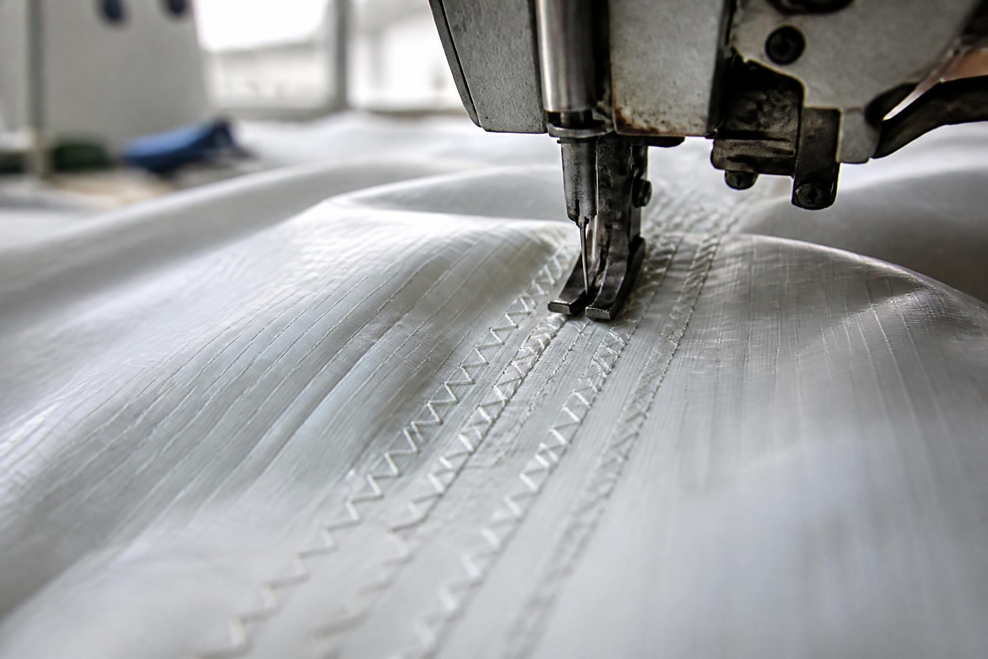 Sailcloth passing under an industrial sewing machine needle in a sailmaking workshop